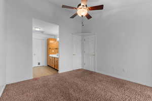 Unfurnished bedroom with a ceiling fan, ensuite bathroom, and light colored carpet