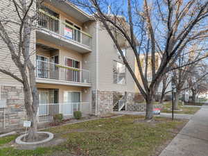 View of side of property featuring stone siding, a lawn, and a balcony