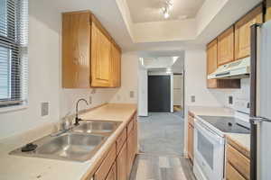 Kitchen featuring white electric range oven, light countertops, freestanding refrigerator, under cabinet range hood, and light wood finished floors