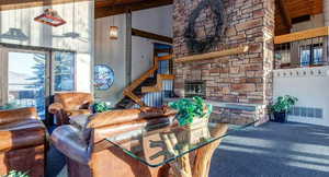 Carpeted living area with a stone fireplace and a high wooden beamed ceiling