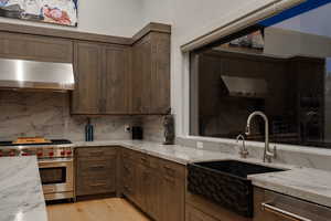 Kitchen featuring appliances with stainless steel finishes, light stone countertops, ventilation hood, and light wood-style floors