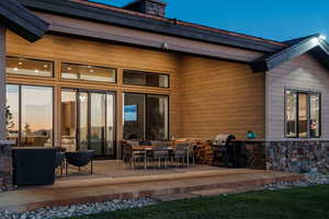 Back of property with outdoor dining area, a patio, and stone siding