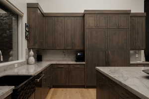 Kitchen with dark brown cabinetry, light stone countertops, backsplash, and light wood finished floors