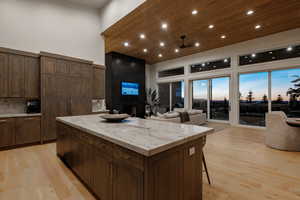 Kitchen with a fireplace, recessed lighting, light wood-style floors, light stone counters, and dark brown cabinetry