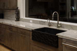 Kitchen featuring dark brown cabinetry, light stone counters, backsplash, and double oven