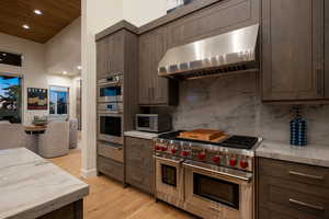 Kitchen with stainless steel appliances, ventilation hood, dark brown cabinets, light wood finished floors, and recessed lighting