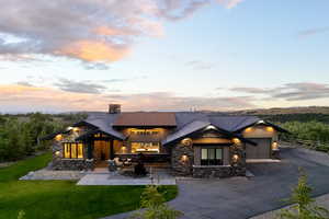 View of front of property with an attached garage, a chimney, stone siding, driveway, and a yard