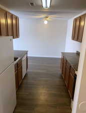 Kitchen with white appliances, dark countertops, brown cabinets, and dark wood-style flooring