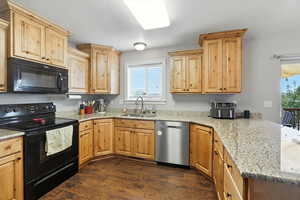 Kitchen featuring black appliances, dark wood-style flooring, a textured ceiling, light stone counters, and light brown cabinetry