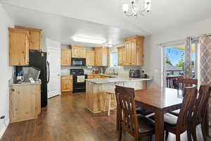Kitchen featuring light brown cabinetry, black appliances, dark wood-style flooring, a peninsula, and light stone countertops