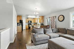 Living room with dark wood-style flooring, a chandelier, and lofted ceiling