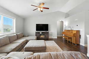 Living room featuring lofted ceiling, dark wood-type flooring, a glass covered fireplace, ceiling fan, and arched walkways