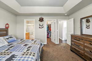 Bedroom featuring dark colored carpet, a raised ceiling, a walk in closet, ensuite bathroom, and a textured ceiling