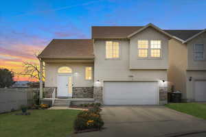 View of front of home with stone siding, an attached garage, concrete driveway, and stucco siding