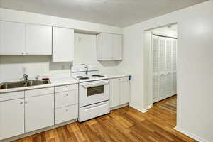 Kitchen with white cabinets, white electric range oven, light countertops, light wood-style floors, and a textured ceiling