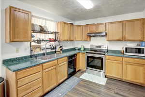 Kitchen with stainless steel range with electric cooktop, a textured ceiling, white microwave, dark countertops, and black dishwasher