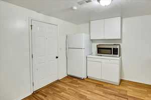 Kitchen featuring white cabinetry, freestanding refrigerator, stainless steel microwave, light wood-type flooring, and light countertops