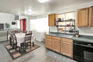 Kitchen with dark countertops, black dishwasher, a textured ceiling, open floor plan, and brown cabinetry