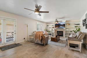 Living area featuring a textured ceiling, a tile fireplace, light wood finished floors, and ceiling fan