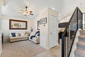 Living room with stairway, vaulted ceiling, light wood-style floors, a decorative wall, and ceiling fan