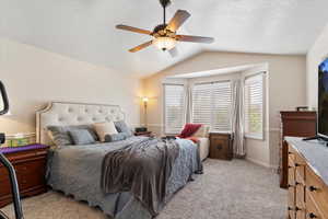 Bedroom with light colored carpet, vaulted ceiling, a textured ceiling, and a ceiling fan