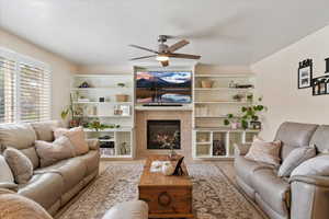 Living area with a fireplace, a ceiling fan, a textured ceiling, and wood finished floors