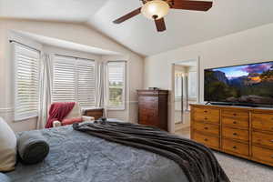 Bedroom with vaulted ceiling, light colored carpet, connected bathroom, and ceiling fan