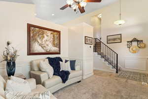 Carpeted living room with wood finished floors, ceiling fan, and stairs