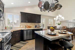 Kitchen with lofted ceiling, a kitchen bar, light stone counters, a kitchen island, and decorative backsplash