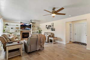 Living room with light wood-style flooring, ceiling fan, a tile fireplace, and a textured ceiling