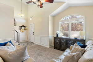 Carpeted living room with ceiling fan, a decorative wall, vaulted ceiling, and wainscoting