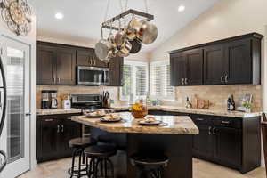 Kitchen featuring light wood-style flooring, a breakfast bar area, stainless steel appliances, backsplash, and vaulted ceiling