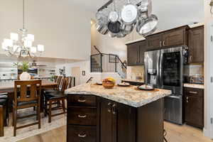 Kitchen featuring dark brown cabinets, a chandelier, stainless steel refrigerator with ice dispenser, backsplash, and a kitchen island