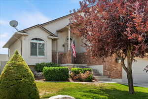View of front facade with brick siding, stucco siding, a front yard, an attached garage, and driveway
