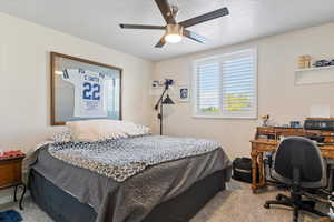 Carpeted bedroom featuring an office area, a textured ceiling, and ceiling fan