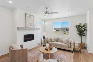 Living area featuring wood finished floors, a glass covered fireplace, recessed lighting, and a ceiling fan