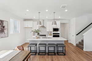 Kitchen with white cabinets, light wood-style floors, light stone countertops, wall chimney range hood, and recessed lighting
