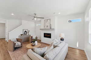 Living room featuring recessed lighting, light wood-style flooring, a glass covered fireplace, and ceiling fan