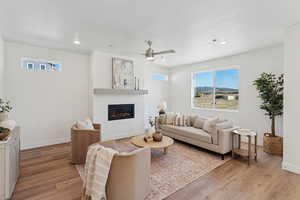 Living room with light wood finished floors, ceiling fan, a glass covered fireplace, and recessed lighting