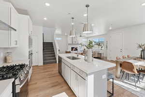 Kitchen featuring white cabinets, stainless steel appliances, light wood-style flooring, hanging light fixtures, and open floor plan