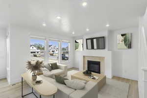 Living room with light wood-style flooring, a glass covered fireplace, and recessed lighting