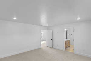 Primary bedroom with light colored carpet, recessed lighting, and connected bathroom