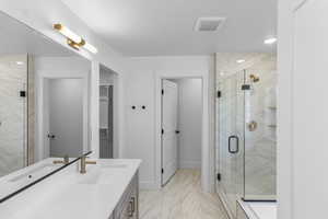 Primary Bathroom featuring a marble finish shower, light marble finish flooring, a walk in closet, vanity, and recessed lighting