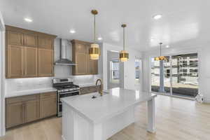 Kitchen with backsplash, gas range, light wood-style flooring, wall chimney exhaust hood, and recessed lighting