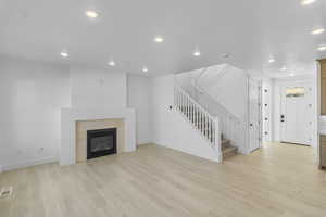 Lliving room with stairway, light wood-type flooring, recessed lighting, and a glass covered fireplace