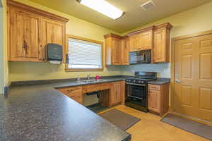 Kitchen with black appliances, dark countertops, brown cabinetry, and a textured ceiling