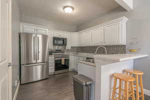 Kitchen with stainless steel appliances, a textured ceiling, decorative backsplash, a breakfast bar, and white cabinets