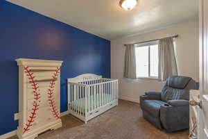 Carpeted bedroom featuring a nursery area and a textured ceiling