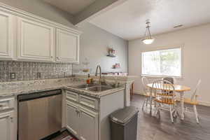 Kitchen featuring tasteful backsplash, stainless steel dishwasher, a peninsula, decorative light fixtures, and a textured ceiling