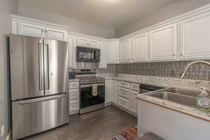 Kitchen featuring appliances with stainless steel finishes, a textured ceiling, white cabinetry, backsplash, and dark wood finished floors